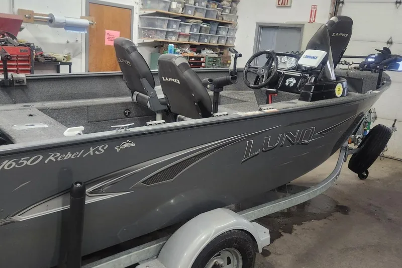 The Image of 2018 Lund 1650 Rebel XS Tiller boat in a garage, featuring dual seats and steering console. - 0