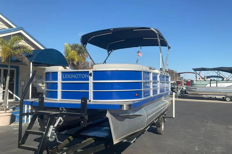 Slide: The Image of 2021 Lexington 318 3 Series pontoon boat on trailer, blue and white design, sunny day. - 3