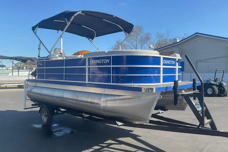 Slide: The Image of 2021 Lexington 318 3 Series pontoon boat on trailer, blue with canopy, parked outdoors. - 5