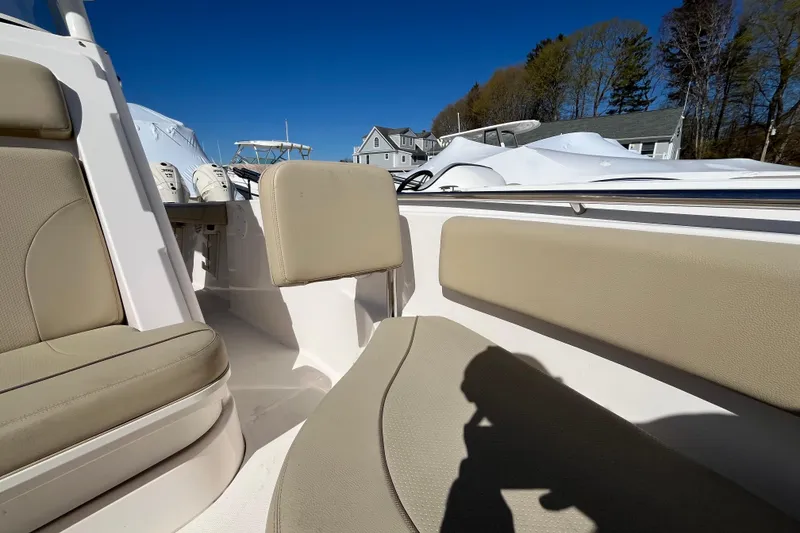 Slide: The Image of 2017 Pursuit C 238 Center Console boat interior with beige seating, docked near houses. - 12