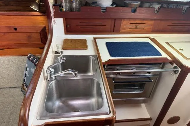 Slide: The Image of 1985 Cape Dory Cutter kitchen with dual sinks, stove, and wooden cabinetry. - 11