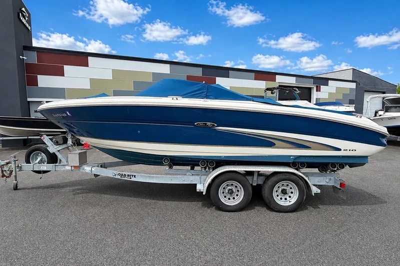 The Image of 2001 Sea Ray 210 Bow Rider boat on trailer, parked outdoors under a blue sky. - 0