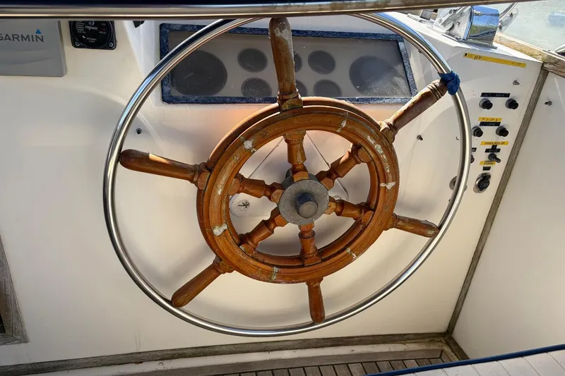 Slide: The Image of Wooden steering wheel of a 1986 Grand Banks 42 Classic yacht, featuring navigation controls. - 14