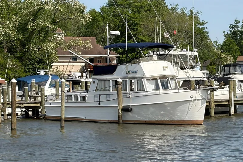 Slide: The Image of 1986 Grand Banks 42 Classic yacht docked at a marina, surrounded by trees and other boats. - 44