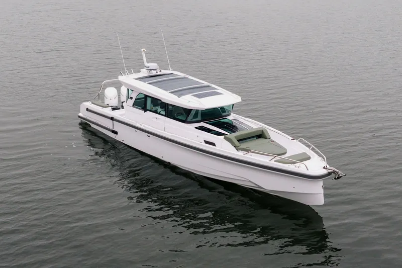 The Image of 2026 Axopar 38 Cross Cabin boat on calm water, surrounded by forested shoreline. - 0