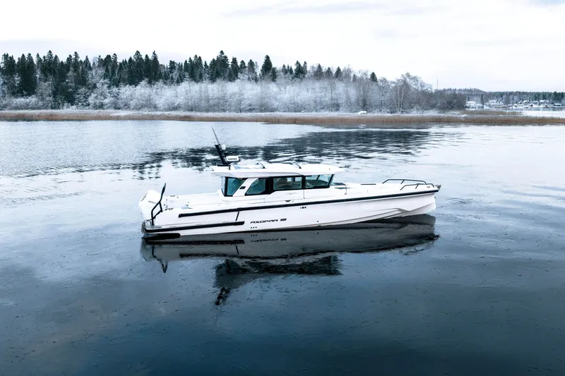 Slide: The Image of 2026 Axopar 38 Cross Cabin boat on a serene, icy lake with snowy forest backdrop. - 7