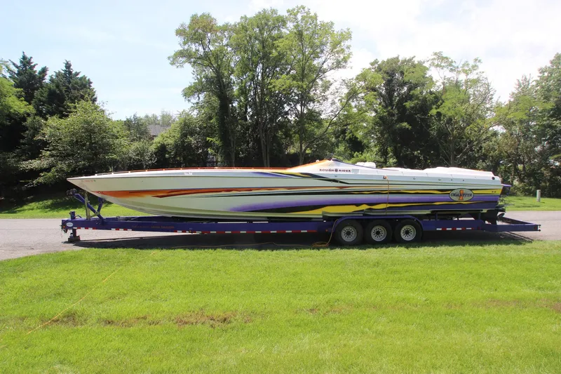 The Image of 2001 Cigarette 46 Rough Rider boat on trailer, vibrant design, parked on grass. - 1