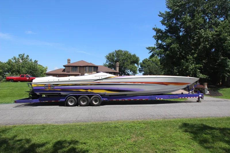 Slide: The Image of 2001 Cigarette 46 Rough Rider boat on trailer, vibrant design, parked in residential area. - 2