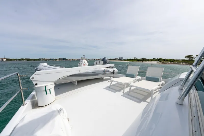 Slide: The Image of 2004 Hatteras 75 Sport Deck Motor Yacht with deck chairs and tender, overlooking coastal waters. - 38