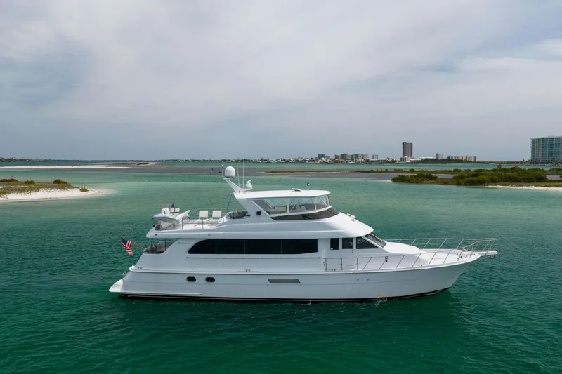 Slide: The Image of 2004 Hatteras 75 Sport Deck Motor Yacht cruising in turquoise waters near a coastal cityscape. - 48
