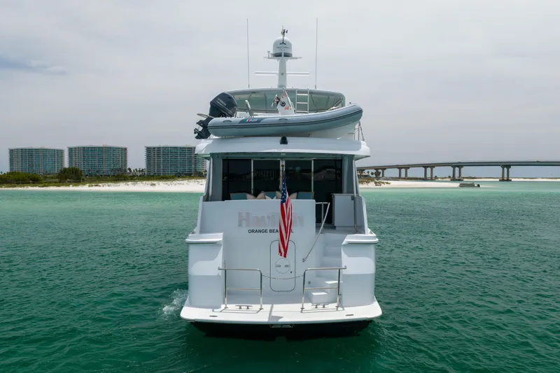 Slide: The Image of 2004 Hatteras 75 Sport Deck Motor Yacht on turquoise waters near a sandy beach and bridge. - 51
