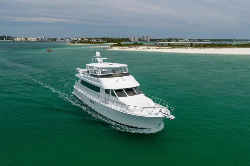 Slide: The Image of 2004 Hatteras 75 Sport Deck Motor Yacht cruising in turquoise waters near a sandy shoreline. - 52