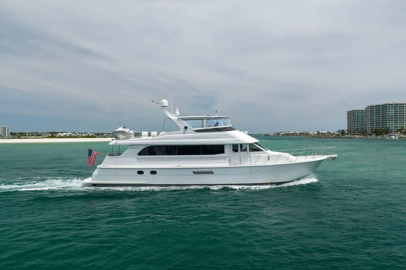 Slide: The Image of 2004 Hatteras 75 Sport Deck Motor Yacht cruising on turquoise waters near a coastal cityscape. - 53
