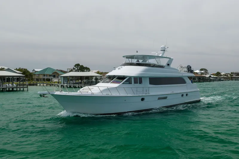 Slide: The Image of 2004 Hatteras 75 Sport Deck Motor Yacht cruising on turquoise waters near docks. - 56