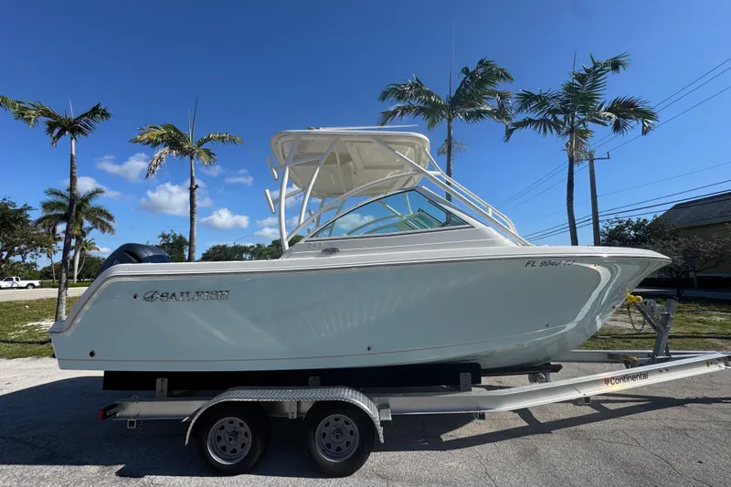 The Image of 2023 Sailfish 245 DC boat on trailer, parked under palm trees, clear blue sky. - 0