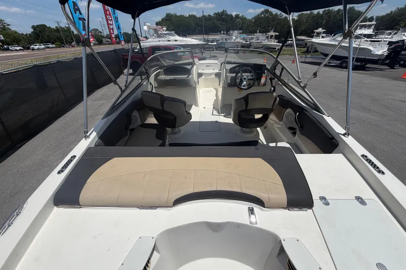 Slide: The Image of 2018 Stingray 204 LR boat interior with seating and steering wheel, parked outdoors. - 11