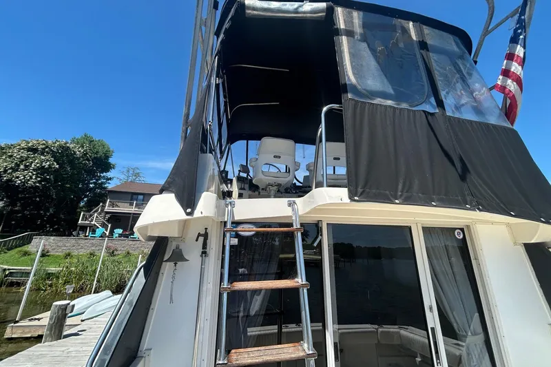 Slide: The Image of 1990 Silverton 34 Convertible boat with ladder and American flag, docked near a house. - 9