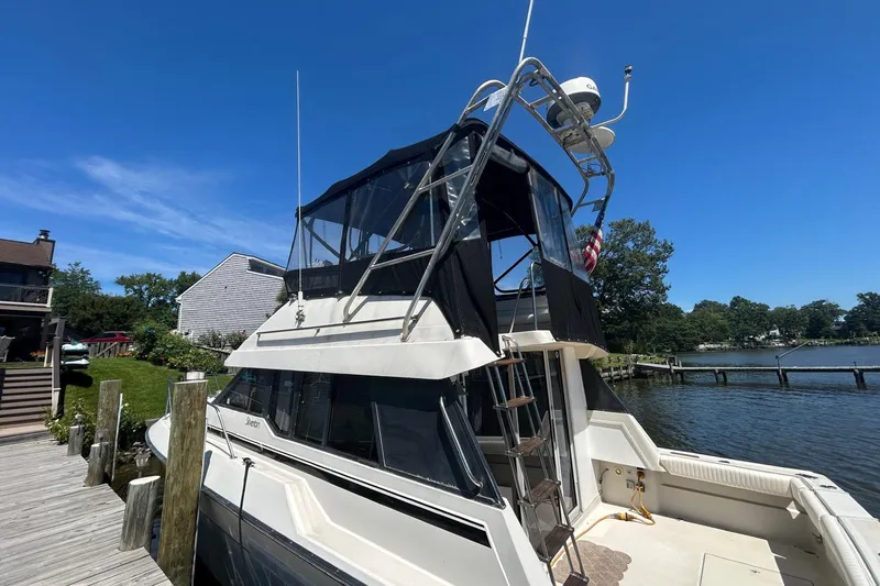 Slide: The Image of 1990 Silverton 34 Convertible boat docked by a serene waterfront under a clear blue sky. - 4