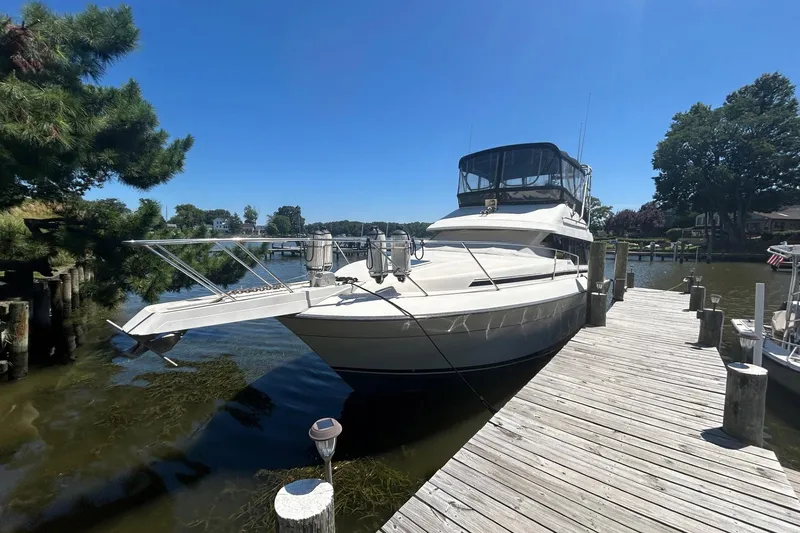 The Image of 1990 Silverton 34 Convertible yacht docked by a wooden pier on a sunny day. - 0