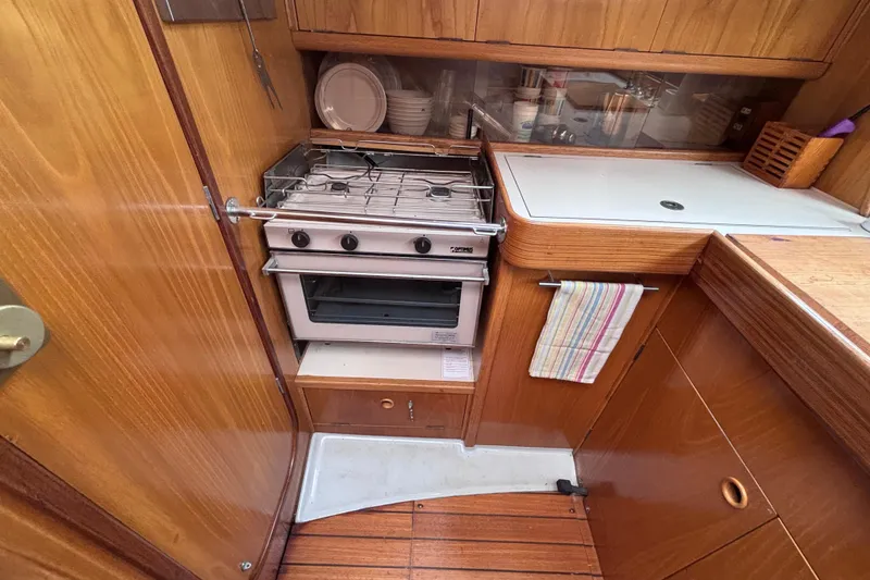 Slide: The Image of Compact kitchen area in a 1990 Beneteau Oceanis 350 sailboat, featuring a stove and wooden cabinetry. - 15