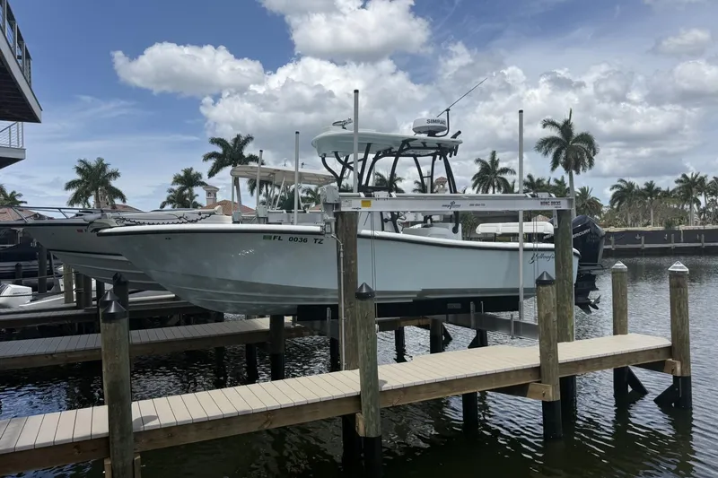 The Image of 2023 Yellowfin 26 Hybrid boat docked by palm trees under a cloudy sky. - 0