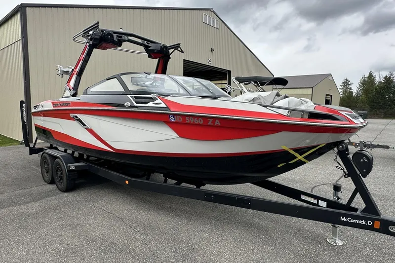 Slide: The Image of 2021 Centurion Ri245 boat in red and white on a trailer, parked near a warehouse. - 3