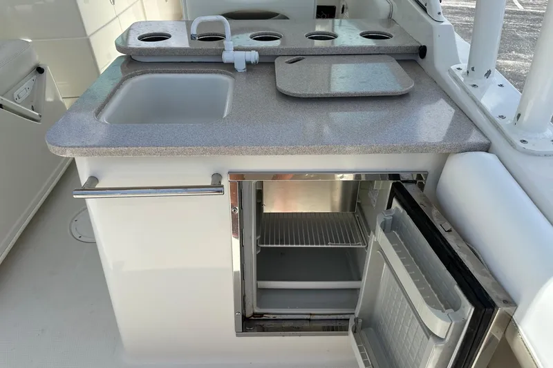 Slide: The Image of 2015 Sailfish 275 DC boat kitchenette with sink, cutting board, and open mini fridge. - 32