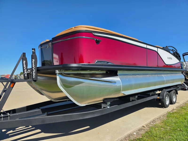 Slide: The Image of A 2027 Harris Sunliner 230 pontoon boat on a trailer, featuring a red hull and silver pontoons. - 1