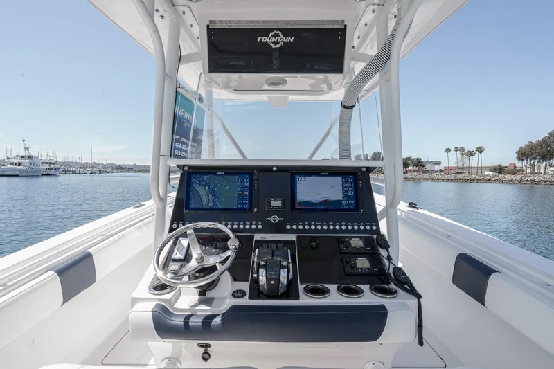 Slide: The Image of 2019 Fountain 38 CC boat dashboard with navigation screens and steering wheel, docked in a marina. - 15