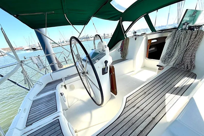 Slide: The Image of 2003 Beneteau 393 sailboat cockpit with green canopy and wooden seating, docked at marina. - 8