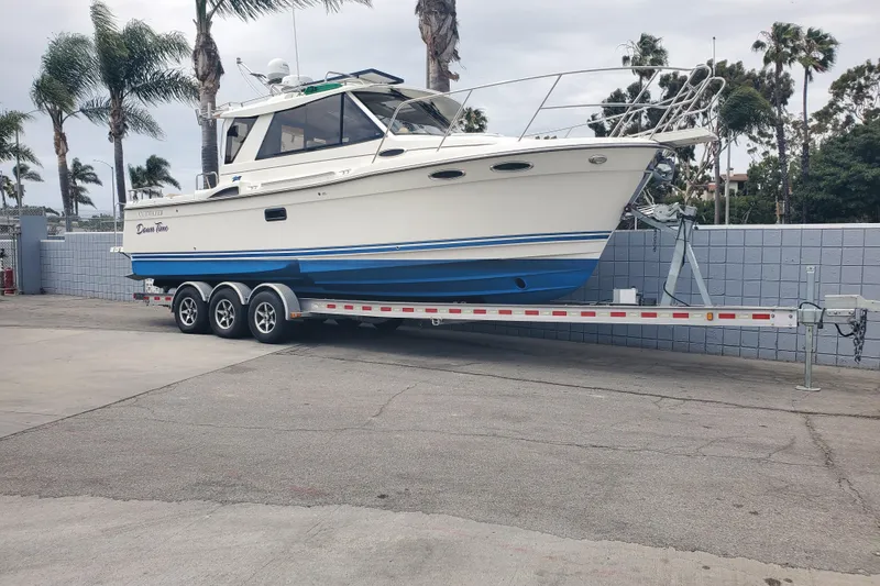 Slide: The Image of 2016 Cutwater 28 boat on trailer, parked near palm trees and a brick wall. - 13