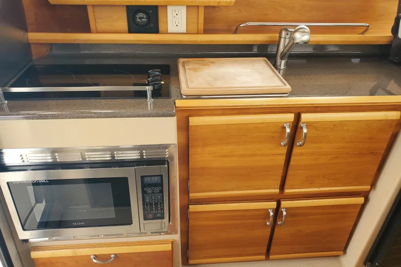 Slide: The Image of 2016 Cutwater 28 galley with stove, microwave, sink, and wooden cabinetry. - 5