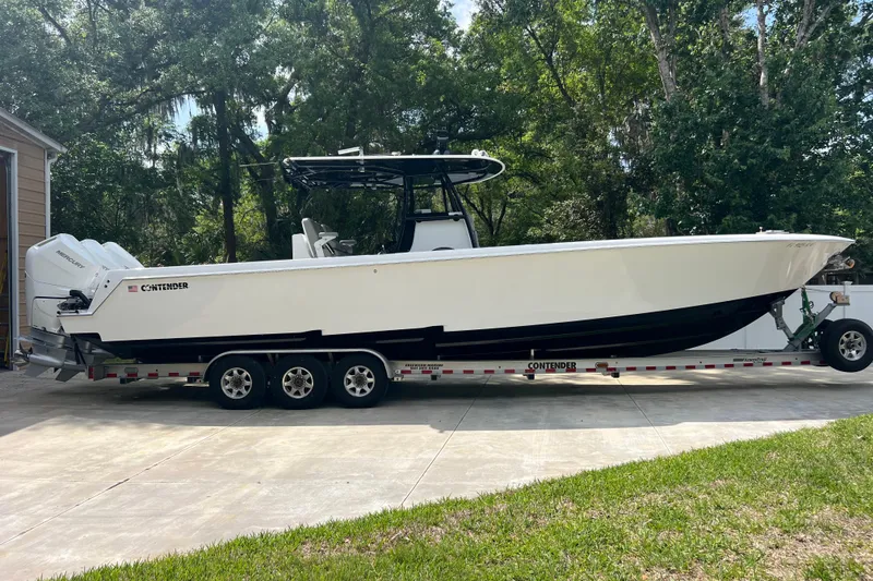 Slide: The Image of 2018 Contender 39 ST boat on trailer, parked in driveway with lush trees in background. - 2