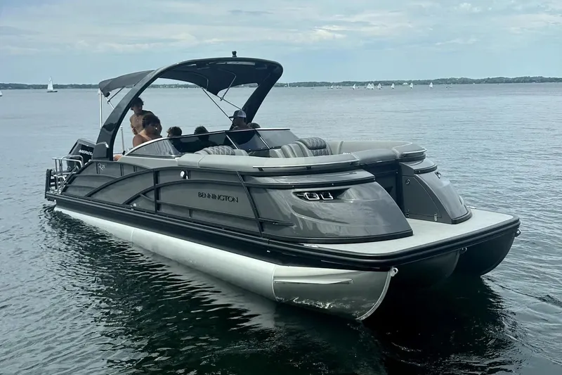 Slide: The Image of 2024 Bennington 25 QSBWA pontoon boat cruising on a calm lake. - 27
