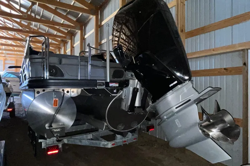 Slide: The Image of 2024 Bennington 25 QSBWA pontoon boat stored indoors, showcasing rear motor and structure. - 56