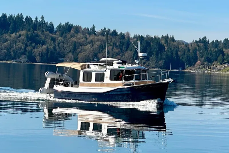 The Image of 2014 Ranger Tugs R-27 cruising on a serene lake with forested shoreline. - 0