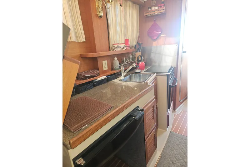 Slide: The Image of 2014 Ranger Tugs R-27 boat kitchen interior with sink, stove, and wooden cabinetry. - 13