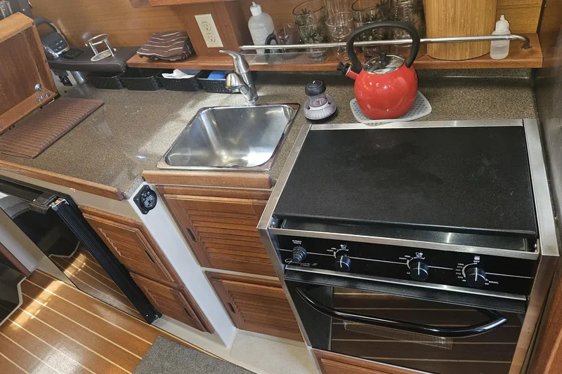 Slide: The Image of Compact kitchen in a 2014 Ranger Tugs R-27 boat with stove, sink, and red kettle. - 14