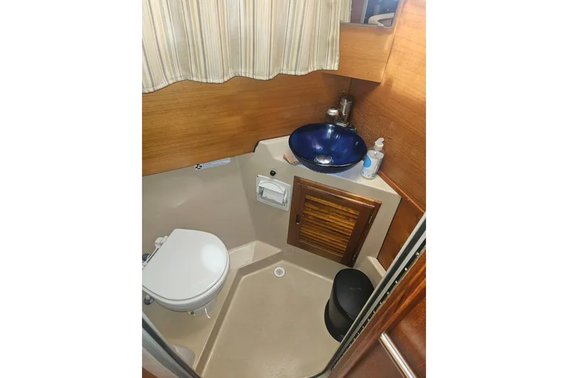 Slide: The Image of 2014 Ranger Tugs R-27 bathroom with blue sink, toilet, and wooden cabinetry. - 20