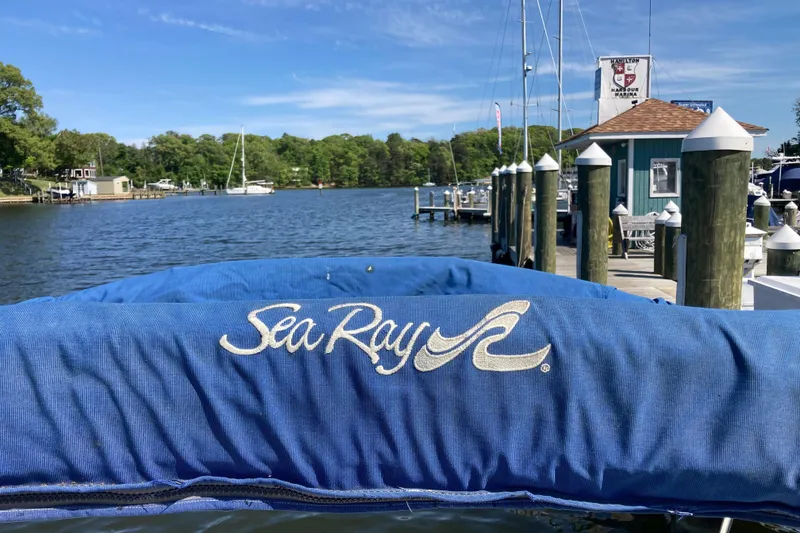 Slide: The Image of Sea Ray Sundancer 260 boat docked at a marina, showcasing blue cover and scenic waterfront. - 48