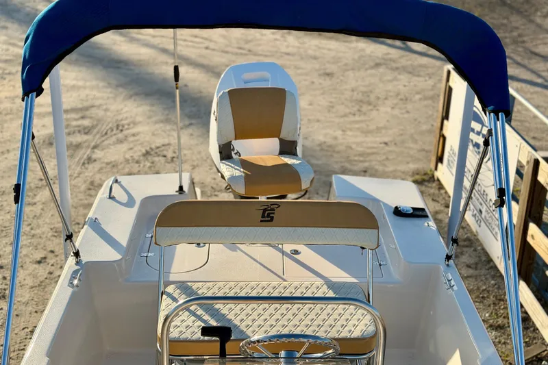 Slide: The Image of 2026 Carolina Skiff 178 JLS boat with blue canopy and beige seating, parked on sandy ground. - 21