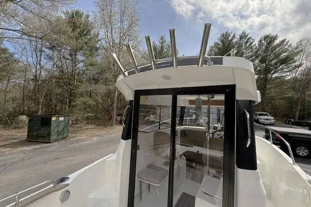 Slide: The Image of 2018 Jeanneau NC Sport 695 boat with rod holders, docked near trees and parked vehicles. - 9