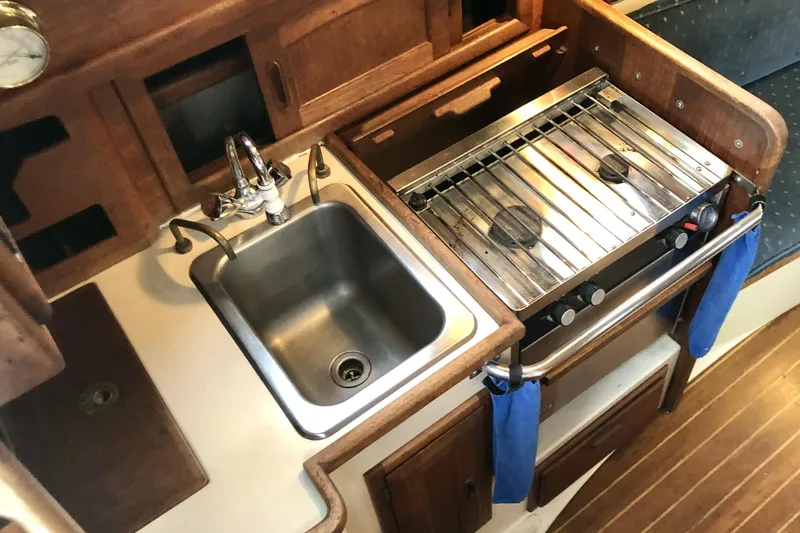 Slide: The Image of 1989 Pacific Seacraft Dana 24 galley with sink and stove, featuring wooden cabinetry. - 9