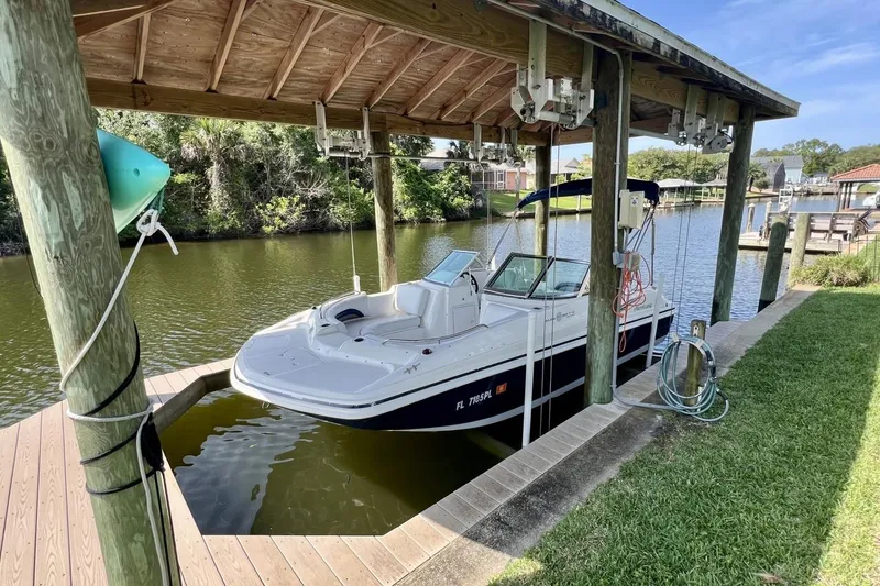 Slide: The Image of 2013 Hurricane SunDeck 187 OB boat docked under a wooden canopy by a serene river. - 64