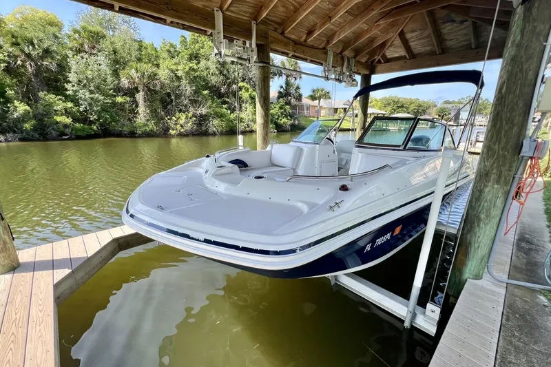 Slide: The Image of 2013 Hurricane SunDeck 187 OB boat docked under a wooden canopy on a calm river. - 65