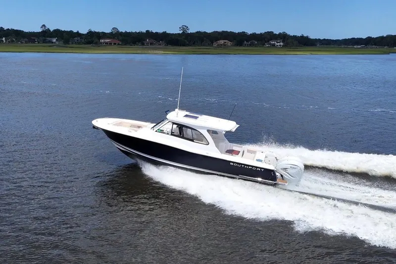 Slide: The Image of 2022 Southport 33 DC boat cruising on a serene lake with lush green shoreline. - 5