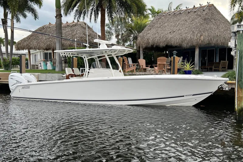 The Image of 2021 Jupiter 34 boat docked by a tropical waterfront with palm trees and thatched roof huts. - 0
