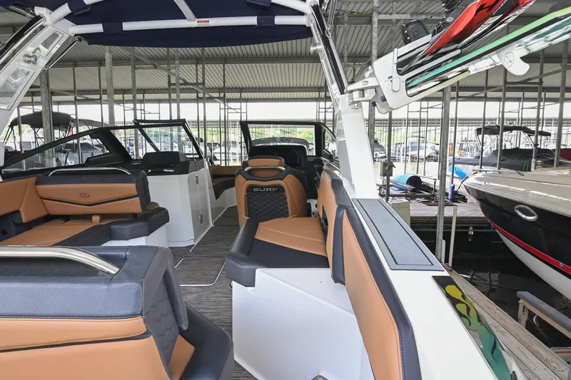 Slide: The Image of 2022 Cobalt R6 Surf boat interior with tan and black seating in a marina. - 12