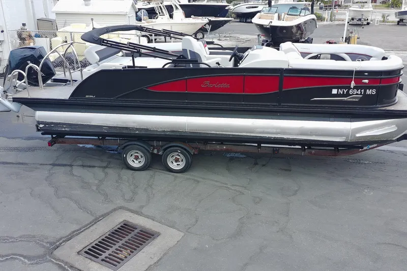 The Image of 2022 Barletta Corsa 23U pontoon boat on trailer, black and red design, parked outdoors. - 0