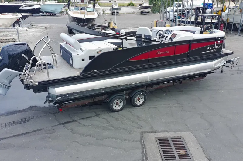 Slide: The Image of 2022 Barletta Corsa 23U pontoon boat on trailer, parked in marina lot. - 2